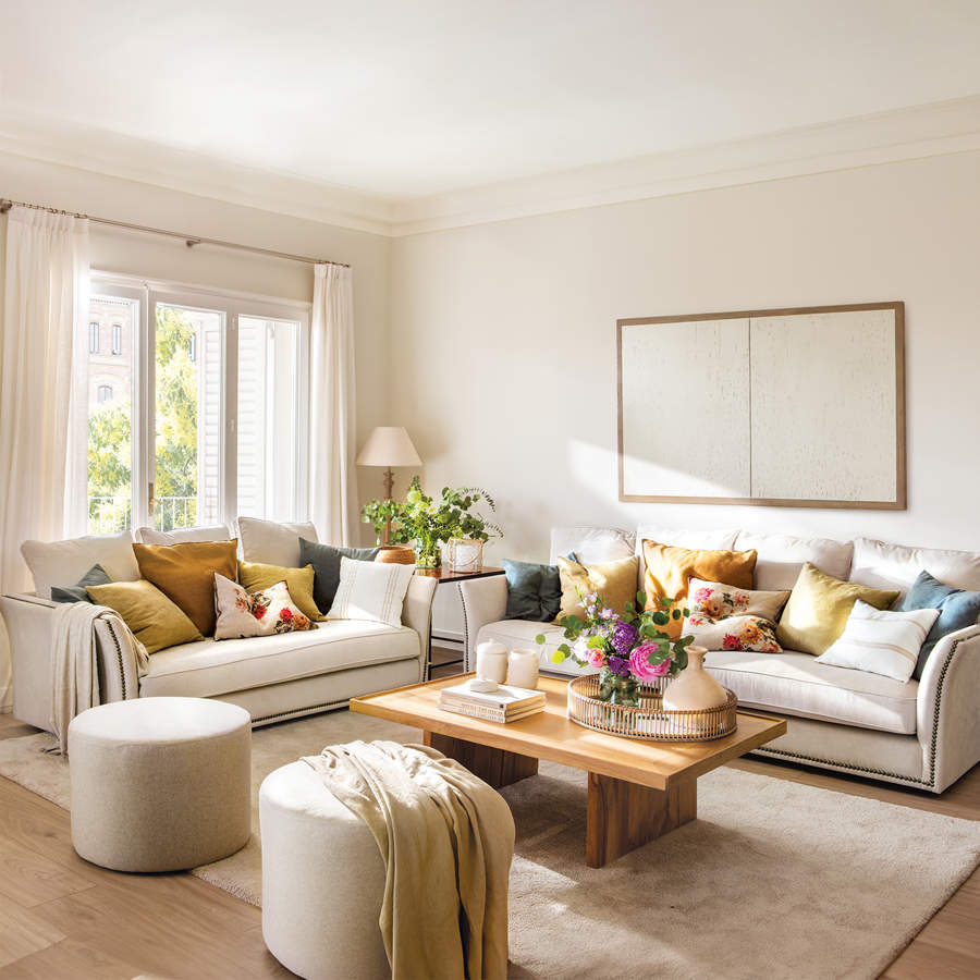 Salón cálido y luminoso con sofás beige y cojines azules, mostaza y floreados